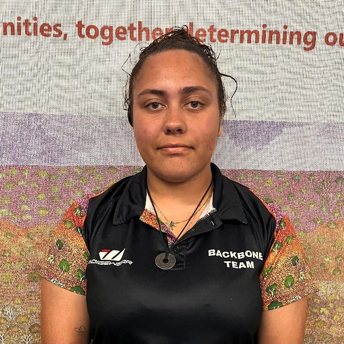 Portrait of a young woman in a black Backbone Team polo with colorful sleeves, standing in front of a banner with text behind her.