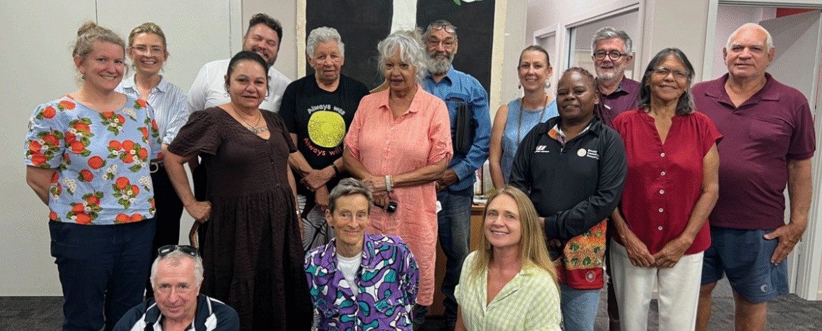 Diverse group of adults posing together for a group photo indoors, smiling at the camera.